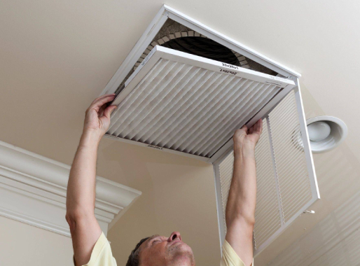 A man is holding an air filter up to the ceiling.